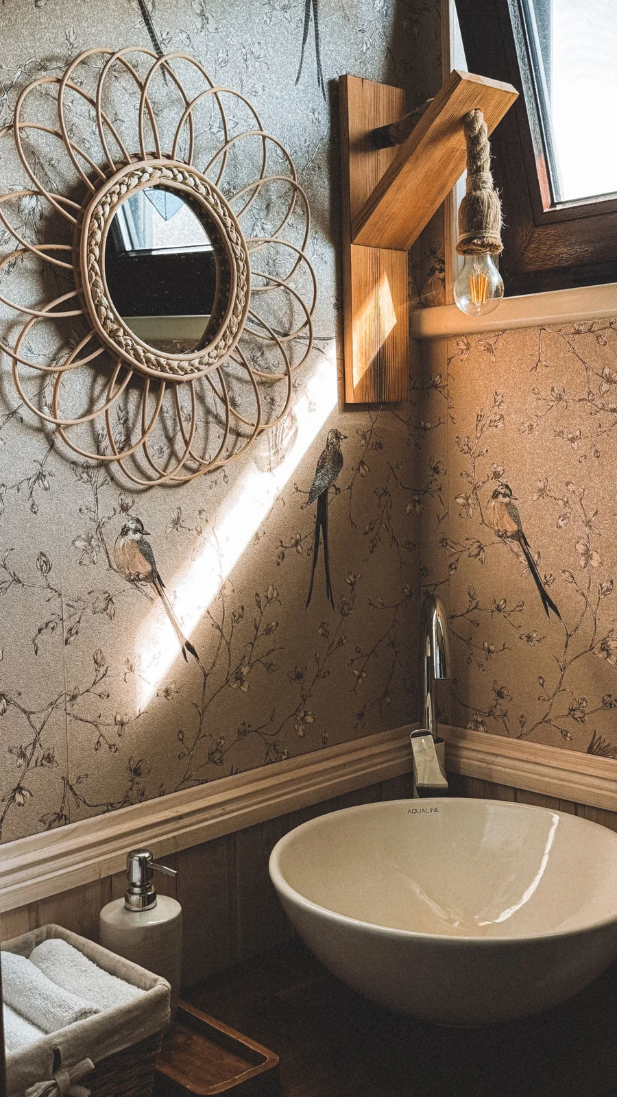 A cozy rustic bathroom featuring a wicker mirror, wall decor, and natural light