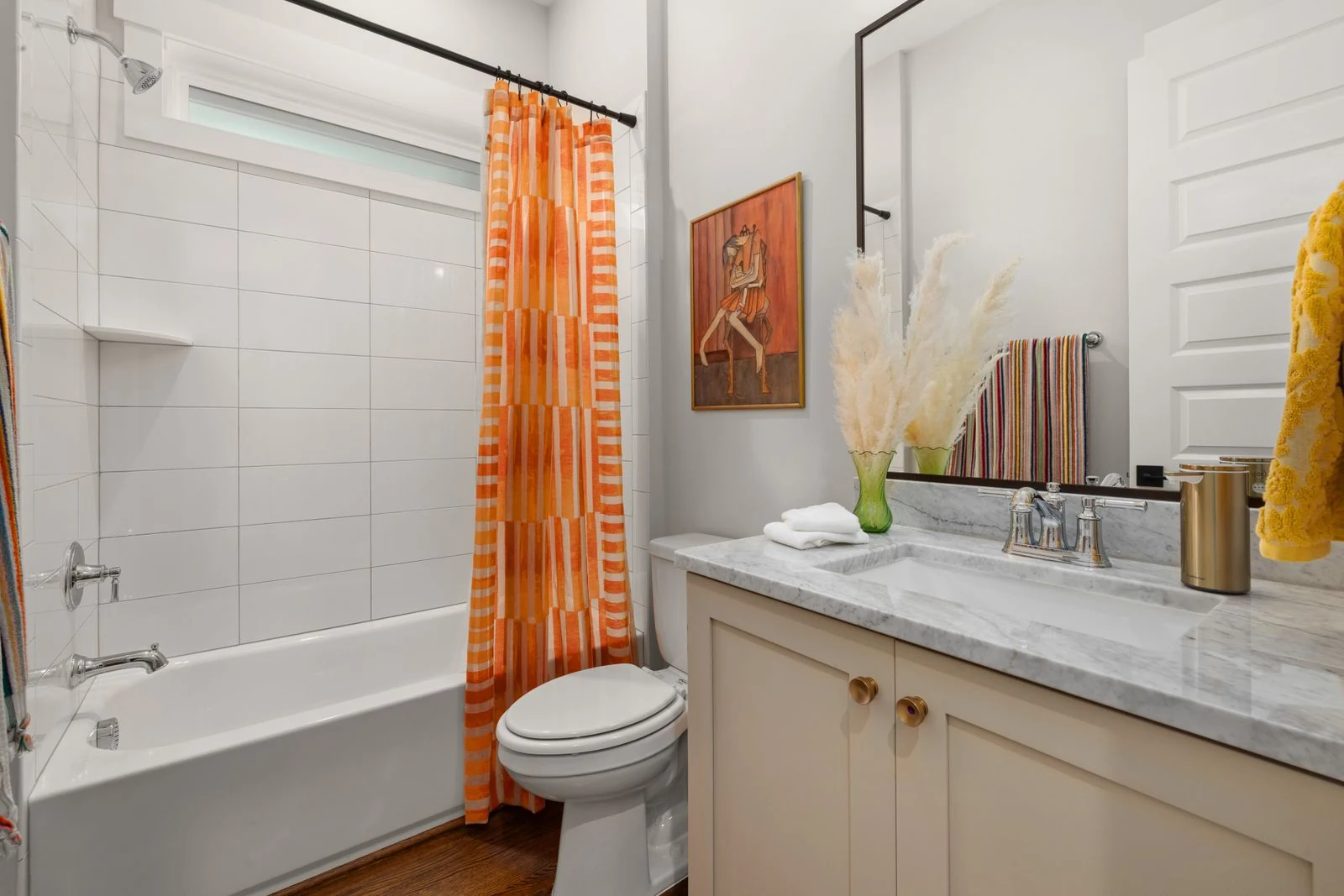 Bright bathroom featuring an orange-striped shower curtain and a marble countertop for a modern look