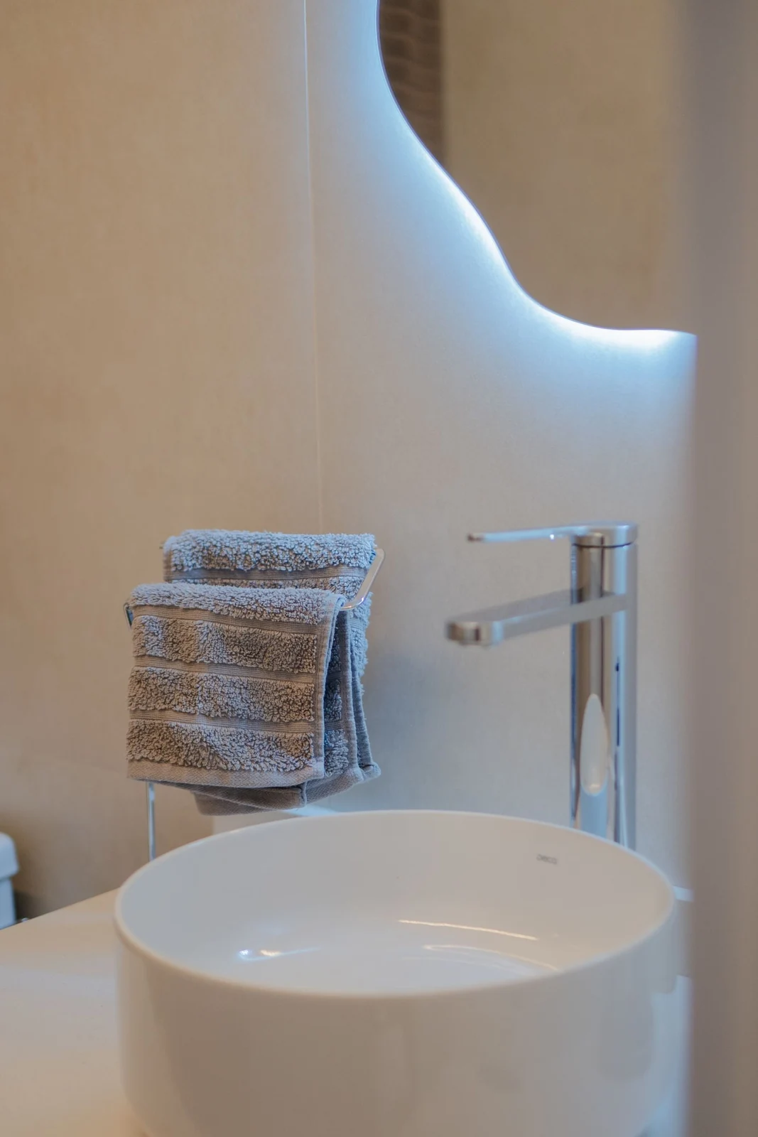 Elegant bathroom with a white ceramic sink and fluffy gray towels beside a sleek faucet