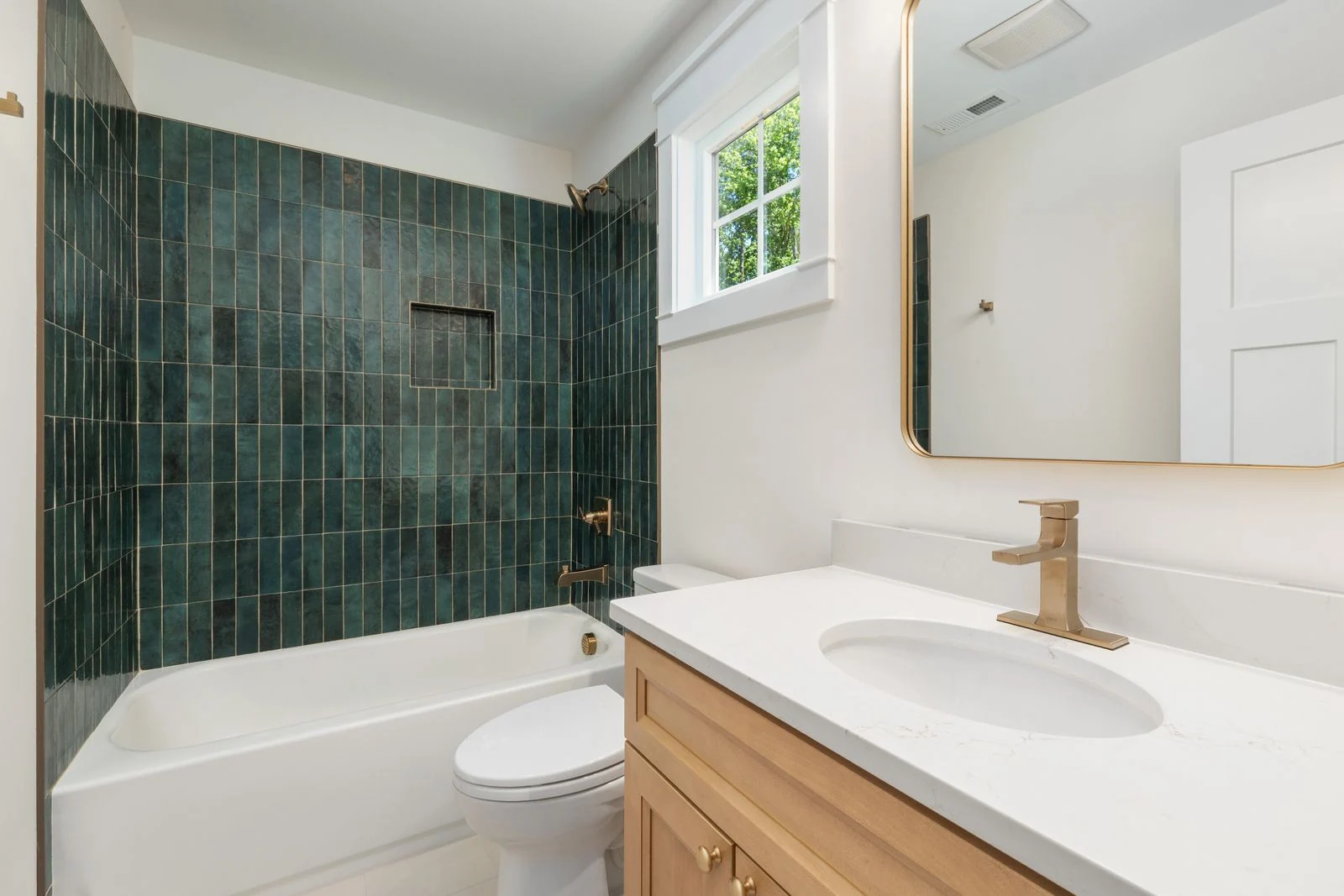 Elegant bathroom featuring a green tiled wall, white tub, and wooden vanity with gold fixtures, offering a modern and stylish look
