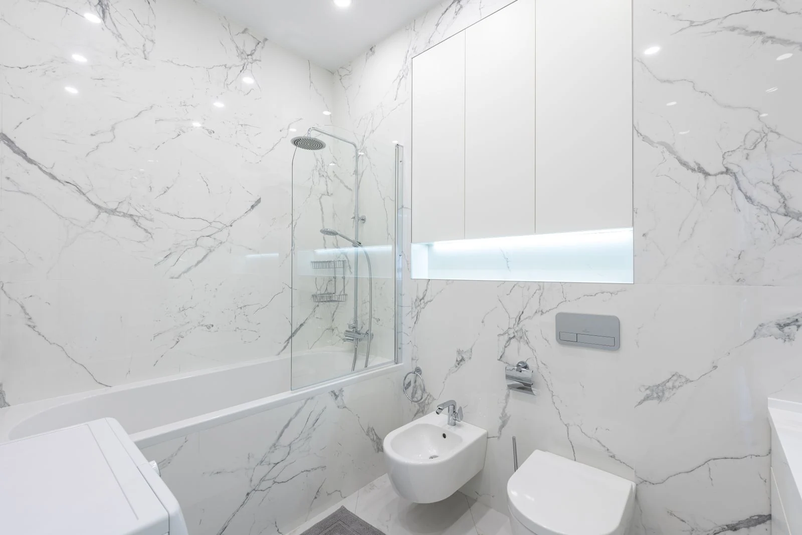 Interior of modern bathroom with toilet and bidet under mirror on white tile next to bathtub with shower