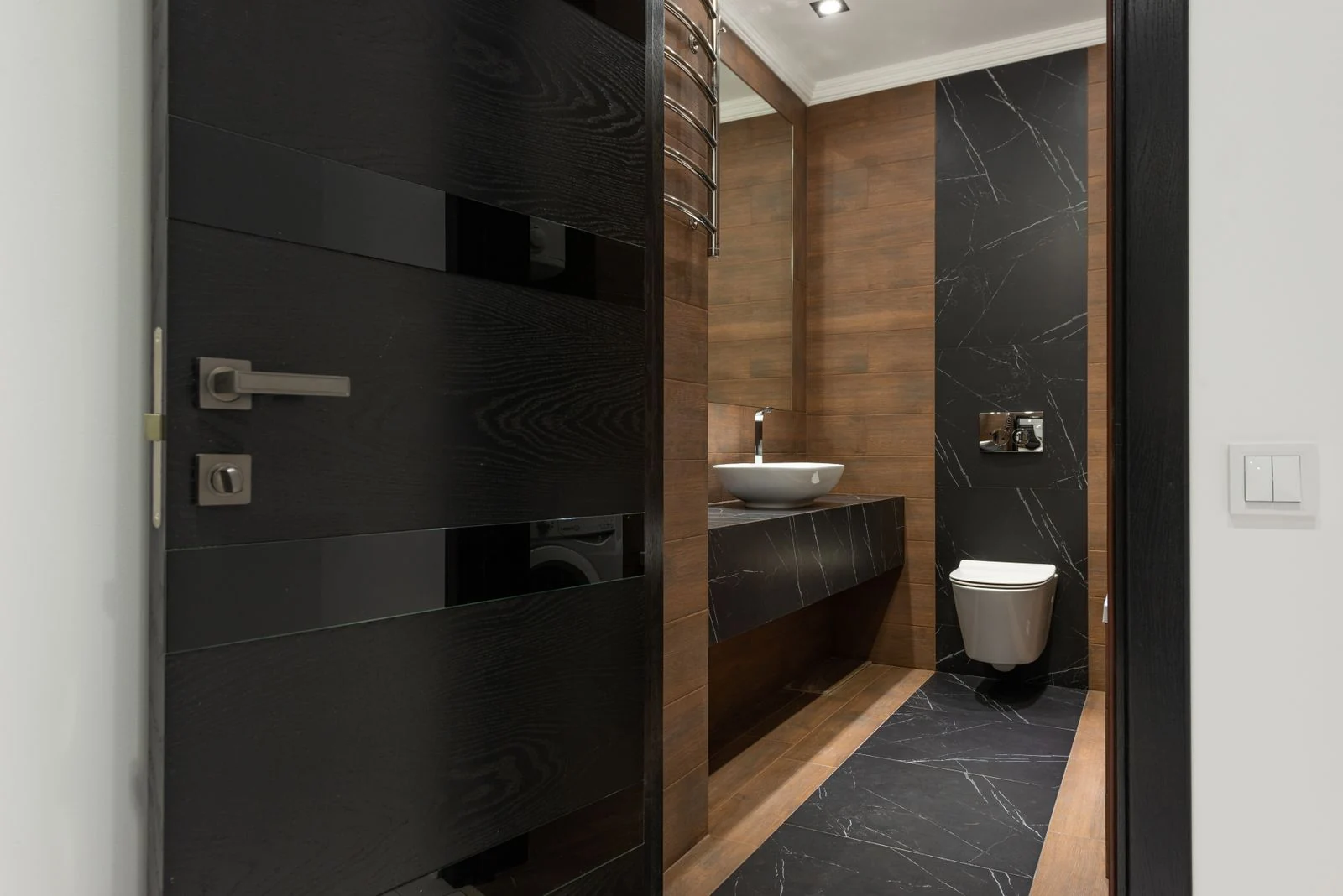 Sleek bathroom with black marble tiles and wooden accents, featuring a modern sink and toilet