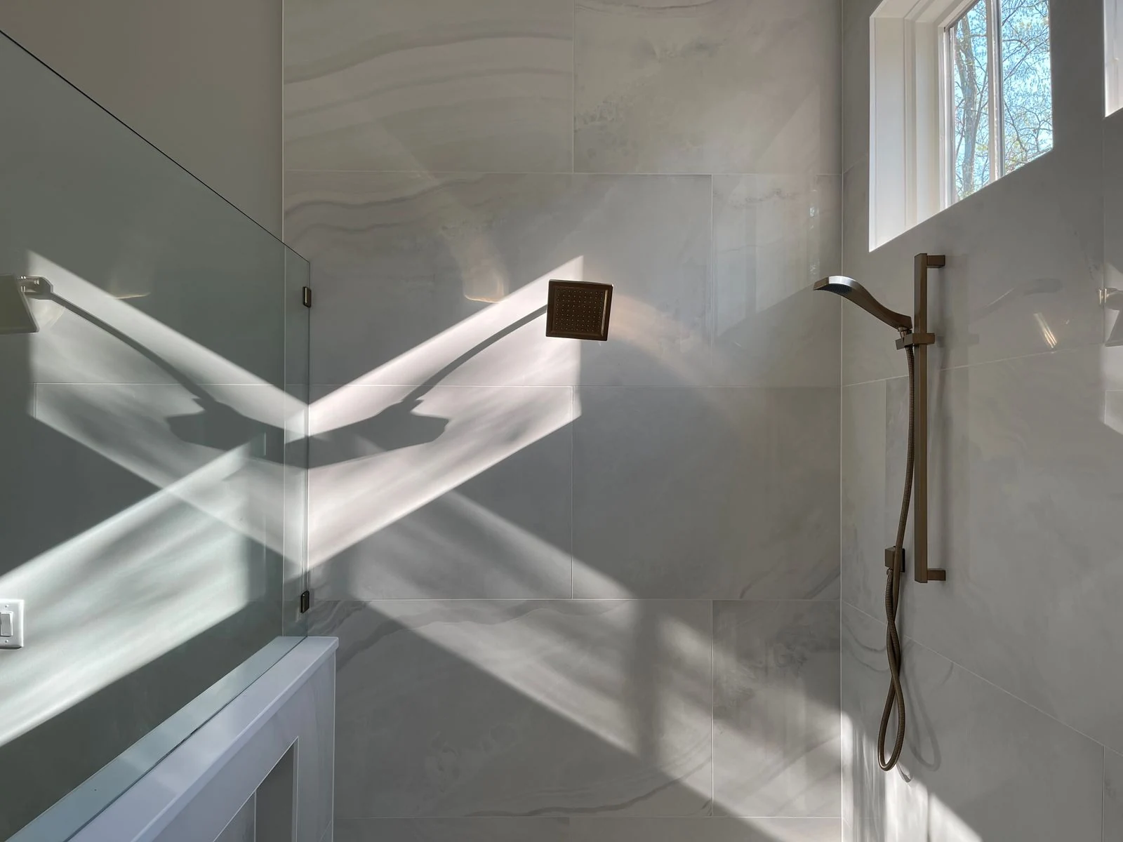 Elegant minimalist bathroom showcasing sunlit reflections on marble tiles and shower fixtures